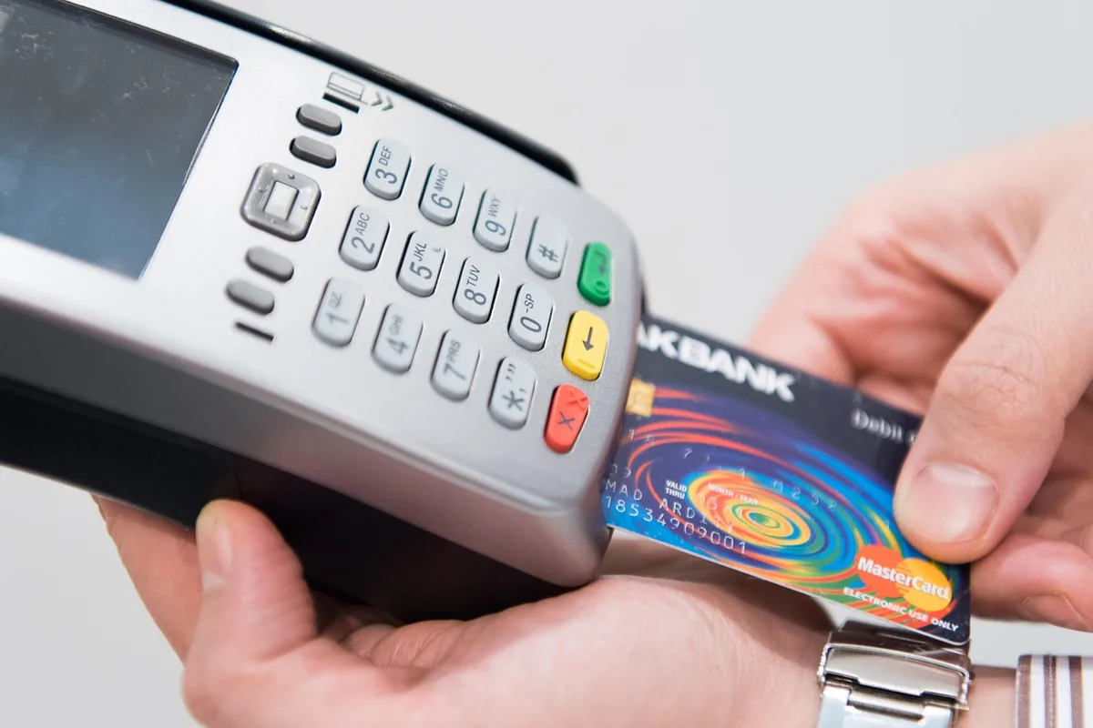 Main tenant une carte bancaire près d'une valise et d'un passeport