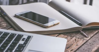 Acheteur anonyme utilisant smartphone et ordinateur portable pour finaliser une commande sur un bureau ensoleillé