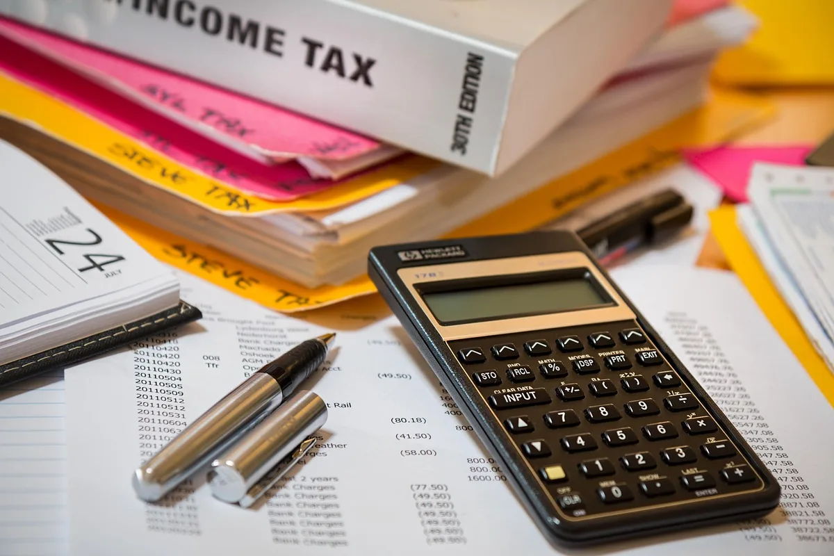 Main déposant de l'argent sur un livret, calculatrice et carnets d'épargne sur une table