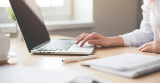 Bureau en journée avec cahier de comptes, ordinateur portable et mains sur une checklist